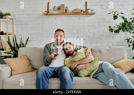 Un couple d'hommes barbus se relaxant et appréciant la compagnie des autres sur le dessus d'un canapé élégant dans un salon. Banque D'Images