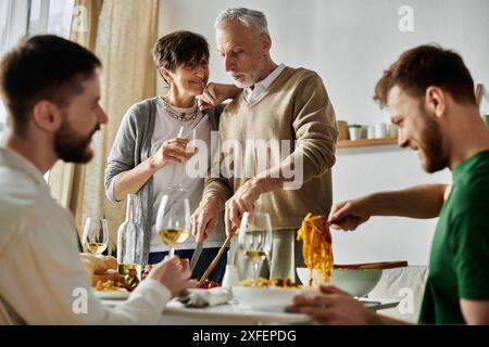 Un couple gay partage un repas avec les parents dans un cadre familial. Banque D'Images