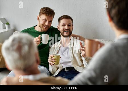 Un couple gay s'assoit sur un canapé avec les parents, profitant du café et de la conversation. Banque D'Images