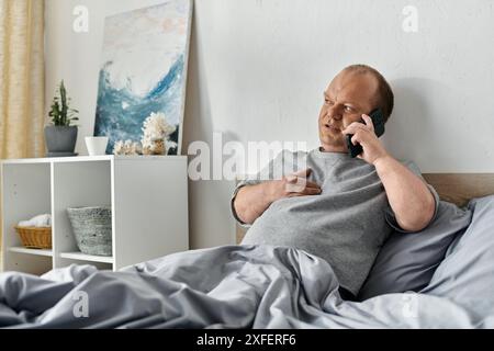 Un homme avec inclusivité est assis dans son lit parlant au téléphone. Banque D'Images