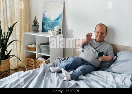 Un homme avec inclusivité est assis sur un lit agitant à un téléphone. Banque D'Images