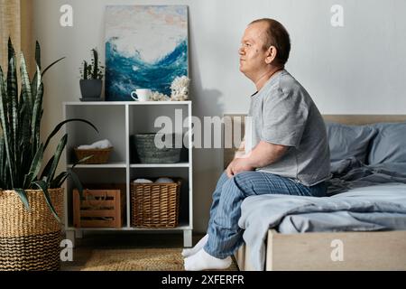 Un homme avec inclusivité est assis sur le bord d'un lit, regardant introspectif. Banque D'Images