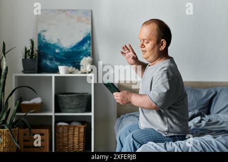 Un homme inclusif est assis sur son lit et utilise son téléphone pour passer un appel vidéo. Banque D'Images