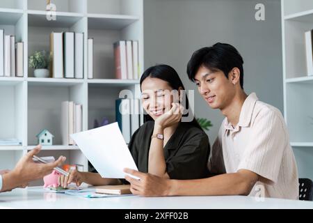 Un couple joyeux est assis à une table, examinant les documents financiers et planifiant leur avenir ensemble dans un cadre moderne. Banque D'Images