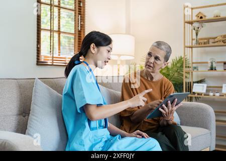 Un professionnel de la santé en gommages bleus assiste une femme âgée à la maison, en utilisant une tablette numérique pour des soins médicaux personnalisés et un soutien. Banque D'Images