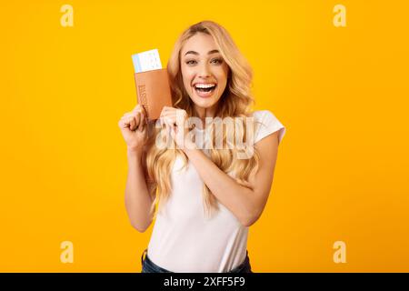 Jeune femme excitée détenant un passeport et une carte d'embarquement contre Yellow Banque D'Images
