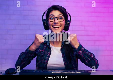 Femme de jeu excitée portant des écouteurs et des lunettes après avoir gagné Banque D'Images