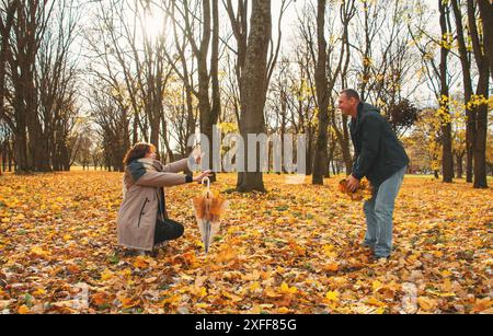 un couple marié de plus de 50 ans, marchant dans le parc en automne par une chaude journée ensoleillée, jouant avec les feuilles qui tombent et riant, passant une journée de congé Banque D'Images