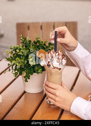 Milkshake avec crème fouettée et sauce au chocolat surmonté d'une gaufrette ion une table en bois d'un café de rue Banque D'Images