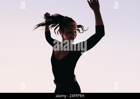 Femme heureuse avec un physique tonique danse expressivement. Son mouvement de corps silhouette et ses bras levés mettent en valeur son style artistique. Banque D'Images