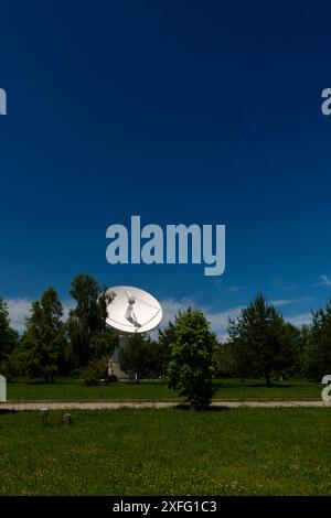 Antenne de radiotélescope blanche dans un champ vert sous un ciel dégagé. Banque D'Images