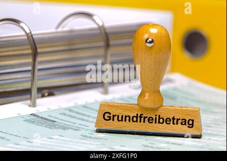 Steuerfreibetrag und Grundfreibetrag Auf einem Aktenordner mit Formularen steht ein Holzstempel mit dem Aufdruck : Grundfreibetrag *** Tax-free allowan Banque D'Images