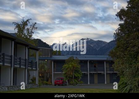 Un hôtel sur main Road dans la petite ville de Franz Josef en Nouvelle-Zélande au coucher du soleil. Les montagnes enneigées et le glacier peuvent être vus au loin Banque D'Images