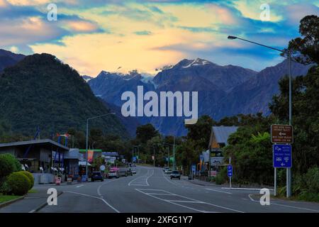 Magasins sur main Road dans la petite ville de Franz Josef en Nouvelle-Zélande au coucher du soleil. Les montagnes enneigées et le glacier peuvent être vus au loin Banque D'Images