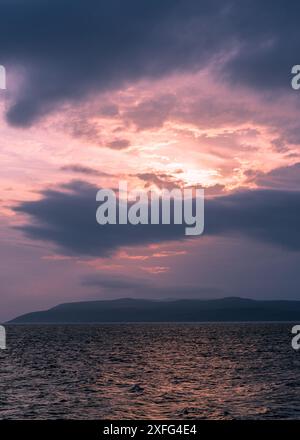 C'est un paysage d'un coucher de soleil rouge-orange d'été avec des nuages sombres sur la plage. La mer, à l'horizon les contours des montagnes peuvent être utilisés comme Banque D'Images