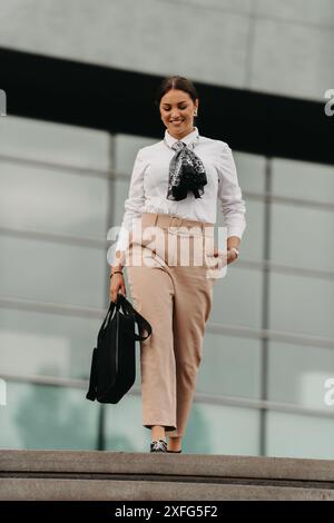 Une femme d'affaires latina souriante marche avec confiance dans les rues urbaines. Banque D'Images