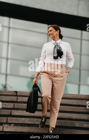 Une femme d'affaires latina souriante marche avec confiance dans les rues urbaines. Banque D'Images