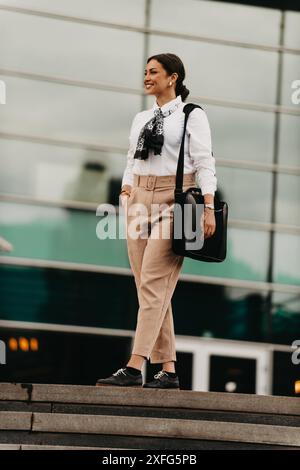 Une femme d'affaires latina souriante marche avec confiance dans les rues urbaines. Banque D'Images