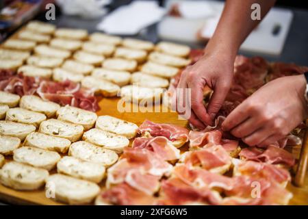 Préparation de canapés pour l'événement de célébration. Mains féminines mettant du jambon de Parme sur une baguette tranchée. Coiffure alimentaire Banque D'Images