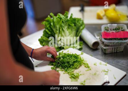 Femme hachant la salade de laitue au couteau sur une planche à découper dans la cuisine. Préparer des aliments pour une alimentation saine Banque D'Images