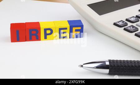 Écrit IRPEF en italien (impôt sur le revenu des particuliers), un seul mot écrit sur des cubes en bois, feuille de papier blanche et calculatrice et stylo sur le bureau. Banque D'Images