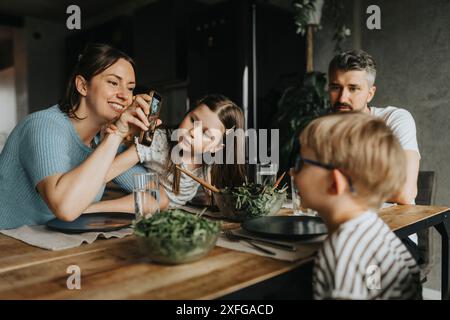 Heureuse mère montrant le téléphone intelligent à son fils tout en ayant de la nourriture à la table à manger Banque D'Images