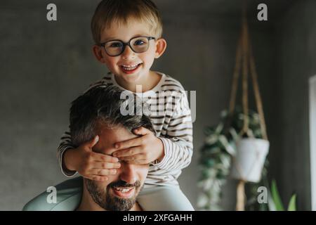 Portrait d'un garçon souriant couvrant les yeux du père tout en étant assis sur l'épaule Banque D'Images