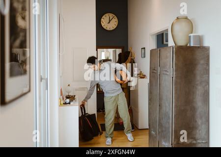 Adolescent gardant le sac sur le sol tout en tenant le basket à la maison Banque D'Images