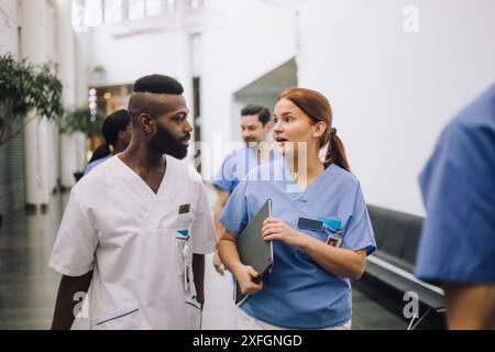 Équipe d'experts médicaux masculins et féminins discutant tout en marchant dans le hall de l'hôpital Banque D'Images