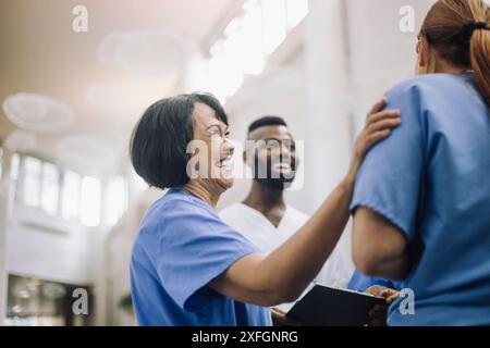Vue latérale d'un médecin senior heureux avec la main sur l'épaule d'un collègue à l'hôpital Banque D'Images