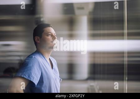 Docteur masculin mature regardant à travers la fenêtre de verre à l'hôpital Banque D'Images