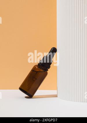 Sérum cosmétique vitamine C en flacon de verre brun avec pipette compte-gouttes sur fond blanc et orange pastel. Concept de cosmétiques de beauté. Soin naturel de la peau Banque D'Images