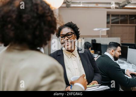 Heureuse femme d'affaires mature parlant avec un collègue tout en se tenant dans le bureau Banque D'Images
