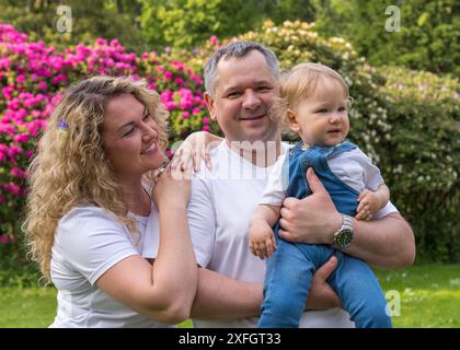 Portrait d'une famille heureuse. Maman avec les cheveux ondulés se tient à côté de papa, tenant un petit enfant d'un an avec les cheveux blonds, une femme regarde doucement le chi Banque D'Images