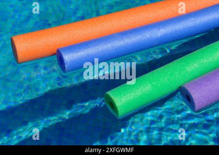 Nouilles de piscine creuses en polyéthylène colorées flottant sur l'eau dans la piscine Banque D'Images