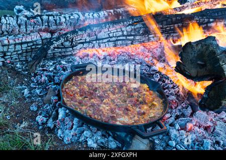 Nourriture faite de légumes, œufs et saucisses cuits dans une poêle au feu de bois. Banque D'Images