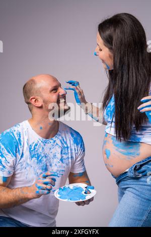 Couple heureux à une soirée de révélation du genre. Un homme et une femme enceinte rient très joyeusement, enduits de peinture bleue parce qu'ils attendent un garçon. Banque D'Images