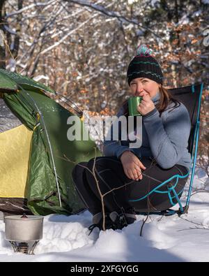 Une femme près de la tente boit du thé. Enroule la corde. Nuit dans la forêt d'hiver. Amour pour la nature. Tourisme écologique. Soleil, forêt, neige. Mode de vie actif . T Banque D'Images