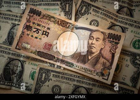 3 juillet 2024, Tokyo, Japon : images d'un billet de 10 000 yens et de billets de 1 dollar américain. Le yen japonais a récemment chuté à son plus bas niveau en 37 ans, tombant en dessous de 160 par rapport au dollar américain. Cette importante dépréciation est la plus faible que le yen ait connue depuis 1986, ce qui a conduit à des attentes accrues d’intervention des autorités japonaises sur le marché. La baisse du yen, qui a atteint 160,82 lors des échanges, a suscité des inquiétudes et des spéculations sur les actions potentielles du ministère japonais des Finances pour stabiliser la monnaie. Cette situation fait suite à des interventions précédentes plus tôt cette année, où Japan sp Banque D'Images