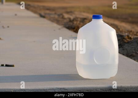 récipient de gallon d'eau plein au quart avec couvercle bleu posé sur le trottoir près de la saleté avec ombre sur le trottoir Banque D'Images