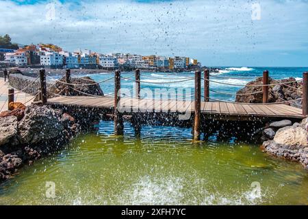 Puerto de la Cruz sur la plage populaire Playa jardin. Un pont en bois derrière une petite cascade. Le village de Punta Brava en arrière-plan. Banque D'Images