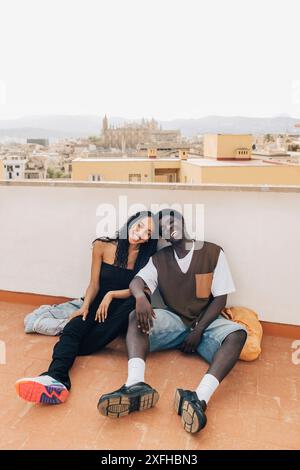 Amis masculins et féminins insouciants assis sur le sol près du mur de soutènement sur le toit Banque D'Images