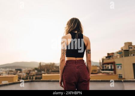 Vue arrière de la jeune femme debout près du mur sur la terrasse du bâtiment Banque D'Images