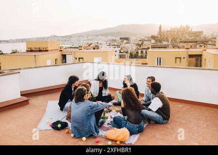 Amis masculins et féminins ayant de la nourriture et des boissons tout en étant assis sur le toit du bâtiment Banque D'Images