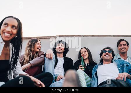Vue à angle bas d'amis masculins et féminins souriants profitant de boissons à la fête sur le toit Banque D'Images