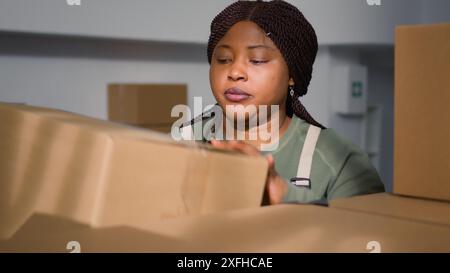 Employé afro-américain dans l'entrepôt manipulant des boîtes en carton pleines de produits prêts à être expédiés aux clients. Travailleur dans la salle de stockage plaçant les colis sur les étagères de l'armoire Banque D'Images