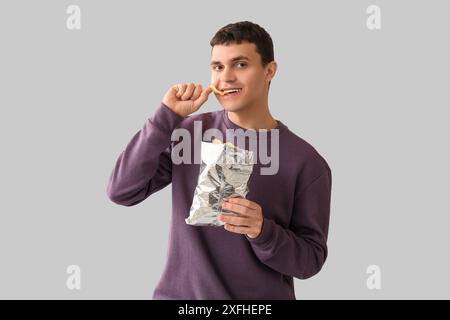 Jeune homme mangeant des chips sur fond clair Banque D'Images