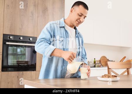 Jeune homme versant le lait de la cruche dans le verre dans la cuisine Banque D'Images