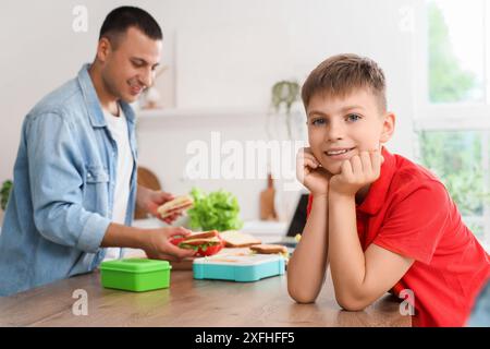 Petit garçon avec son père emballant la boîte à lunch de l'école dans la cuisine Banque D'Images