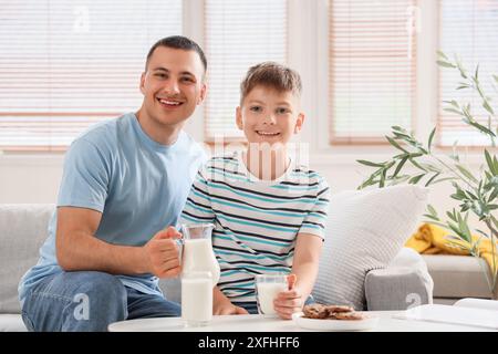 Heureux père avec pichet de lait et son petit fils assis sur le canapé à la maison Banque D'Images